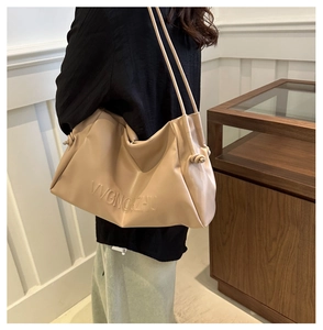 Detail of beige pleated cloud bag showing side knot and embossed brand lettering