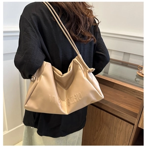 Detail of a beige soft leather hobo bag with embossed lettering on model shoulder