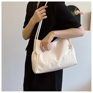 Detalle de bolso tote blanco crema con logo grabado y correas finas con nudos decorativos
