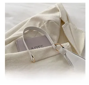 Détail d'un sac demi-lune blanc avec poignée anneau doré posé sur un blazer texturé