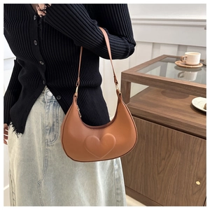 Sac hobo en cuir mat caramel avec relief cœur porté à l'épaule sur une tenue chic