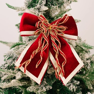 Nœud de Noël en velours rouge avec bordure dorée sur un sapin de Noël enneigé