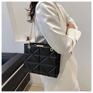 Detail of geometric quilted black chain bag worn over the shoulder with gold hardware