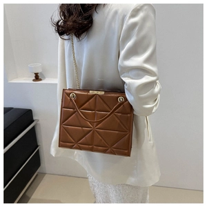 Detail view of brown geometric quilted tote with gold chain strap on a white blazer