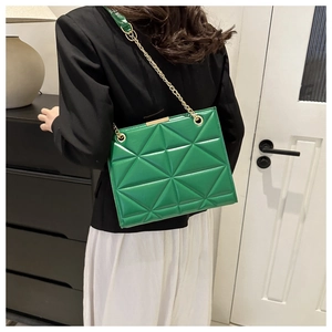 Green quilted tote bag with gold chain strap shown on a shoulder in a home setting