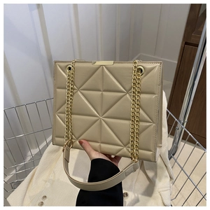 Detail of beige quilted tote bag featuring gold chain strap and geometric stitching