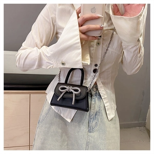 Detail of a black mini crossbody bag with a rhinestone bow and silver chain strap