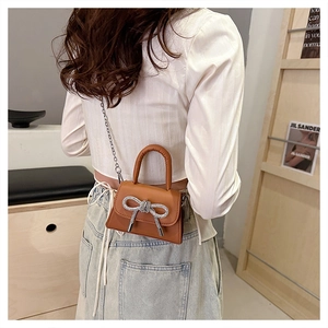 Détail d'un mini sac en cuir marron avec nœud strass et bandoulière en métal
