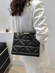 Classic black quilted tote bag with golden chain strap worn by model from behind