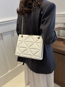 White geometric quilted tote bag with gold chain strap shown on model in grey suit