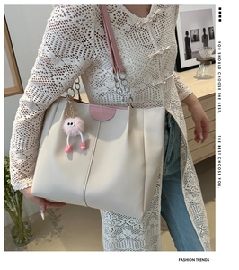 Detail of minimalist cream tote bag with leather tag and plush monster eye charm