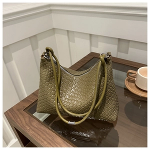 Détail du sac hobo tressé vert olive avec doubles anses sur une table d'appoint