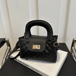 Close-up of black quilted leather handbag with gold metal clasp on a minimal white base