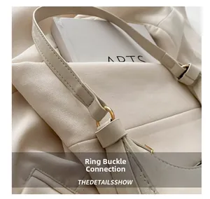 Close-up of golden metal buckle and leather strap on a beige minimalist shoulder bag