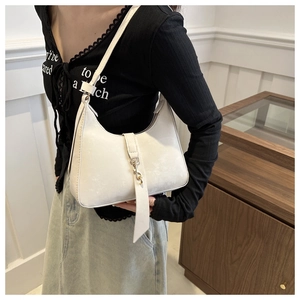 Detail of white hobo bag with gold hardware worn by model in a minimalist setting