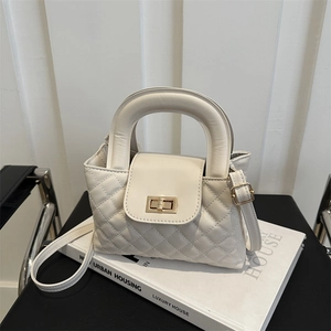 Detail of white quilted handbag featuring gold twist lock and elegant round top handle