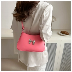 Detail of pink shoulder bag featuring silver metal bow ornament and smooth faux leather