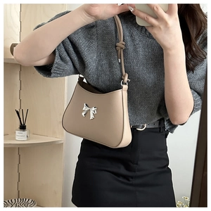 Close-up of beige shoulder bag with silver bow ornament and knotted strap detail