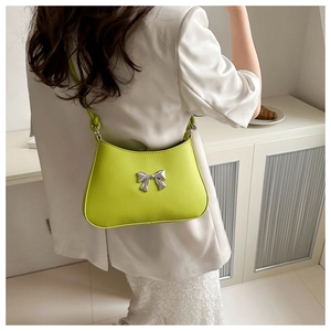 Fashionable bright green shoulder bag with silver metallic bow detail shown on a model