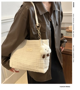 Detail of white textured tote bag with golden rings and plush charm on brown leather jacket
