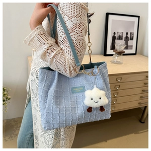 Detail of light blue tweed tote bag with plush cloud charm and gold chain hardware accents