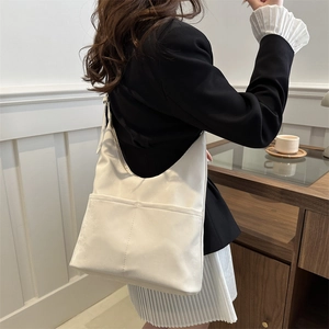 Detail of white hobo shoulder bag with double front pockets on a model in a warm room