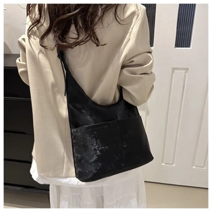 Detail of minimalist black bucket bag with wide front pocket worn by a model in a suit
