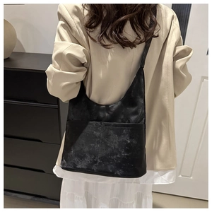 Detail of black matte tote bag with dual front pockets worn over a beige blazer