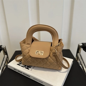 Detail of khaki quilted handbag with gold twist lock and round handle on a white book