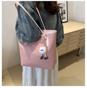Pink woven tote bag with fluffy monster charm and shoulder straps in an indoor setting
