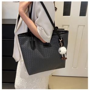Detailed view of black woven tote bag with leather strap and plush charm for women