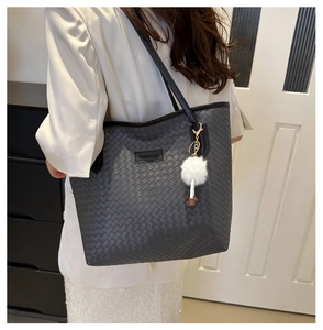 Close-up of grey woven tote bag featuring a black fashion label and white plush pom-pom