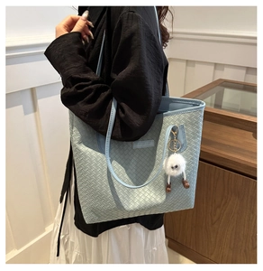 Detail of light blue woven tote bag with minimalist label and cute plush monster charm