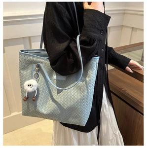 Detail of light blue woven texture tote bag with white plush monster charm accessory