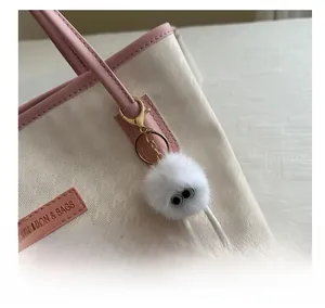 Dettaglio di un ciondolo mostro di peluche bianco con grandi occhi su borsa rosa