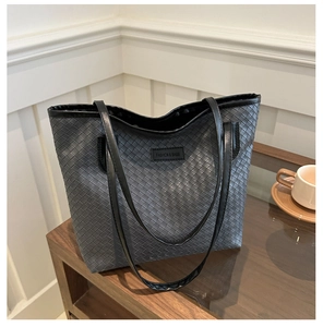 Detail of black woven tote bag with slim straps and fashion logo on a glass coffee table