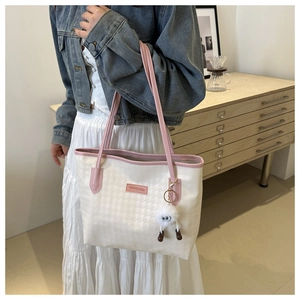 Detailed texture of white houndstooth tote bag with pink straps and plush charm