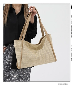 Detail of woven straw tote bag with brown leather handles held by a model in black outfit