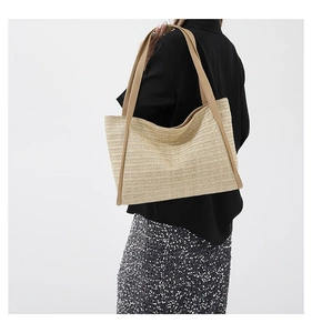 Detail of light beige straw tote bag featuring brown leather shoulder straps and weave texture
