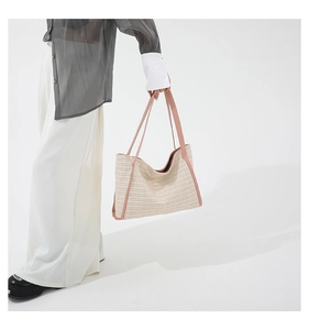 Close-up of model holding beige straw tote bag with pink handles and trim detail