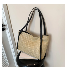Detail of straw woven tote bag featuring black leather straps and natural texture