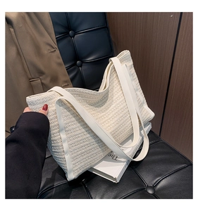 Detail view of woven cream straw tote bag on a dark leather chair with classic texture