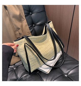 Detail of woven straw tote bag featuring black leather trim and thin shoulder straps