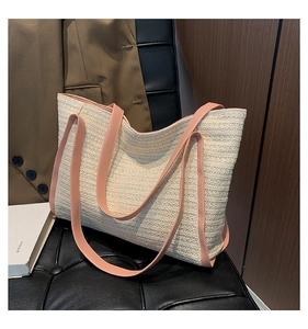 Detail of beige woven tote bag featuring long pink leather shoulder straps on a dark surface