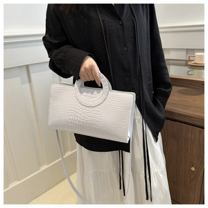 Elegante borsa bianca con trama a coccodrillo e manico circolare in metallo mostrata da modella