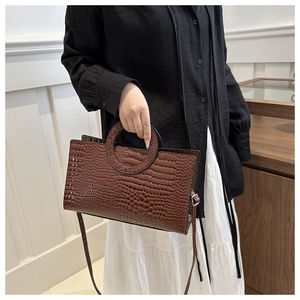 Close-up of brown crocodile pattern handbag with round handles and adjustable strap