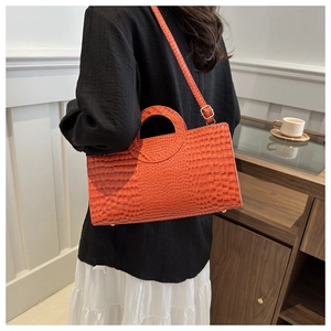 Detail of orange crocodile texture handbag with unique circular cutout handle and strap