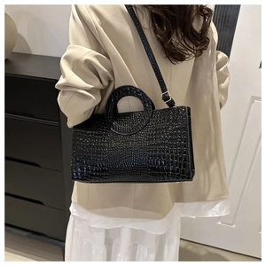 Detail of glossy black crocodile pattern PU handbag with circular cutout handle and gold hardware