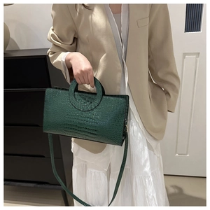 Detail of green crocodile-embossed handbag featuring a unique circular cutout handle design