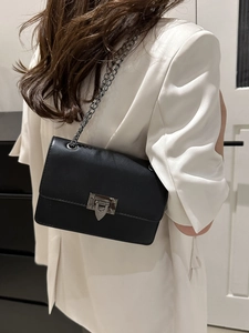 Schwarze Umhängetasche mit Kette und Metallverschluss am Model in modernem Ambiente